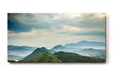 Sinus Art Wandbild 120x80cm Weite grüne Hügel und Berge unter wolkenverhangenem Himmel mit Lichteinfall