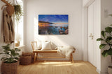 Sinus Art Wandbild 120x80cm Abendliche Szene mit beleuchteter Stadt am Meer, umgeben von Felsen und ruhigem Wasser