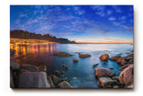 Sinus Art Wandbild 120x80cm Abendliche Szene mit beleuchteter Stadt am Meer, umgeben von Felsen und ruhigem Wasser