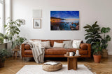 Sinus Art Wandbild 120x80cm Abendliche Szene mit beleuchteter Stadt am Meer, umgeben von Felsen und ruhigem Wasser