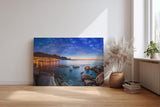 Sinus Art Wandbild 120x80cm Abendliche Szene mit beleuchteter Stadt am Meer, umgeben von Felsen und ruhigem Wasser
