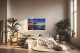 Sinus Art Wandbild 120x80cm Abendliche Szene mit beleuchteter Stadt am Meer, umgeben von Felsen und ruhigem Wasser
