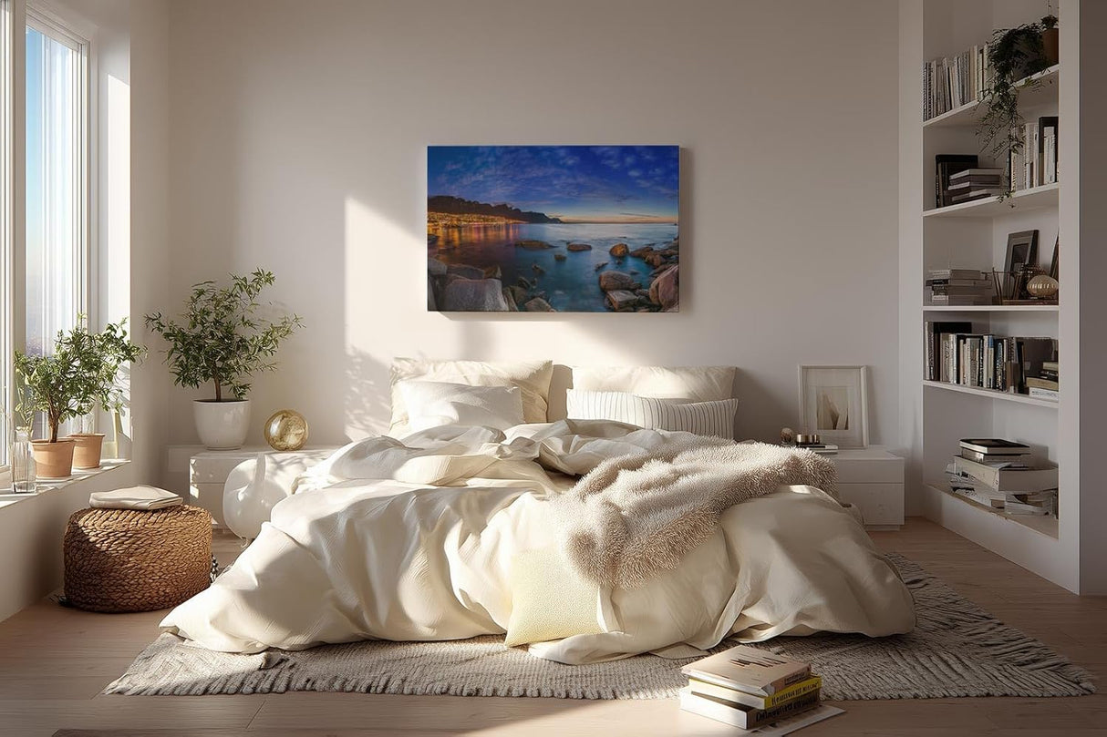 Sinus Art Wandbild 120x80cm Abendliche Szene mit beleuchteter Stadt am Meer, umgeben von Felsen und ruhigem Wasser