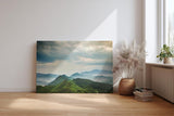 Sinus Art Wandbild 120x80cm Weite grüne Hügel und Berge unter wolkenverhangenem Himmel mit Lichteinfall