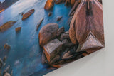 Sinus Art Wandbild 120x80cm Abendliche Szene mit beleuchteter Stadt am Meer, umgeben von Felsen und ruhigem Wasser